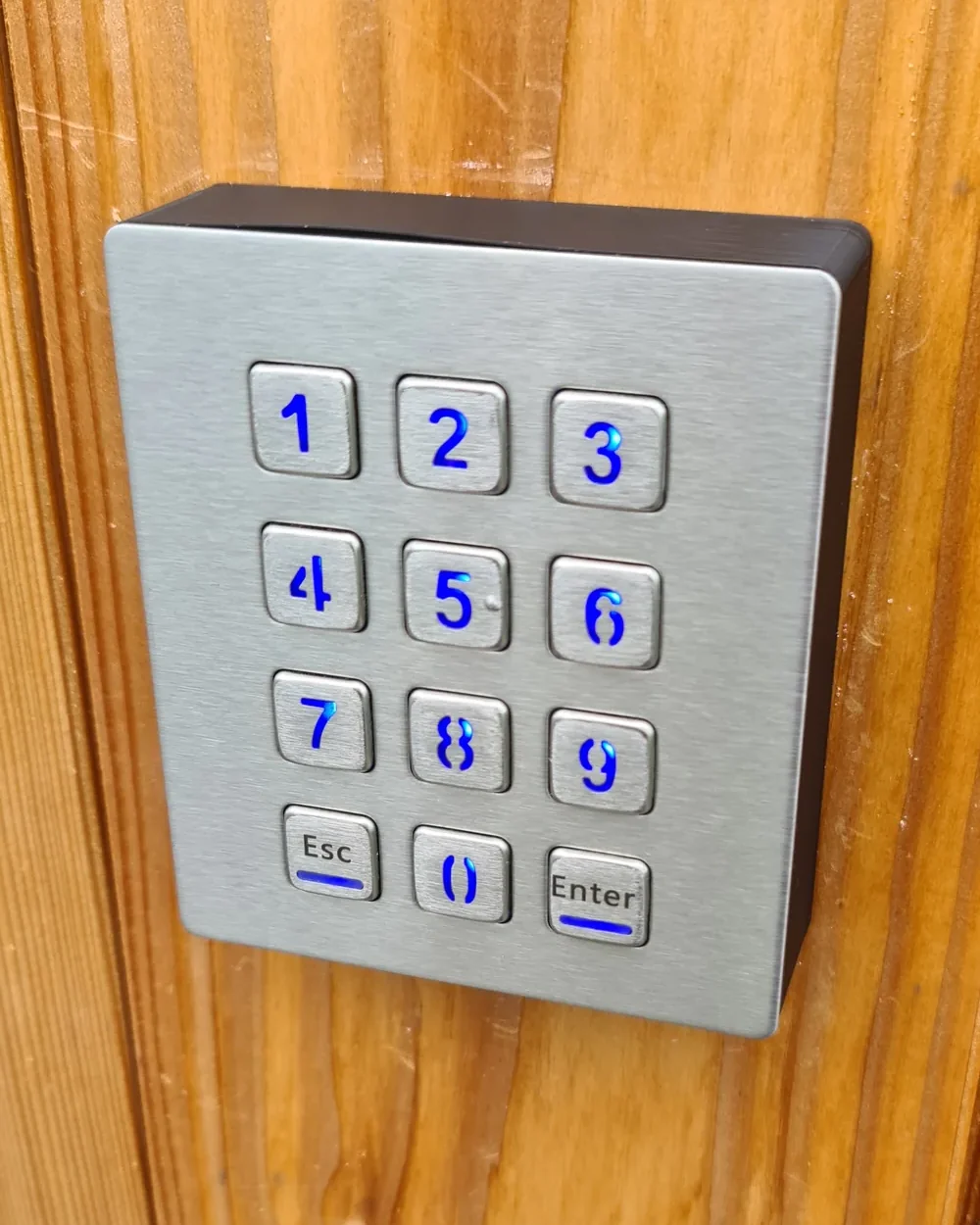 D-Lock Keypad aus Edelstahl mit blau beleuchteten Tasten, montiert an einer Holzfassade